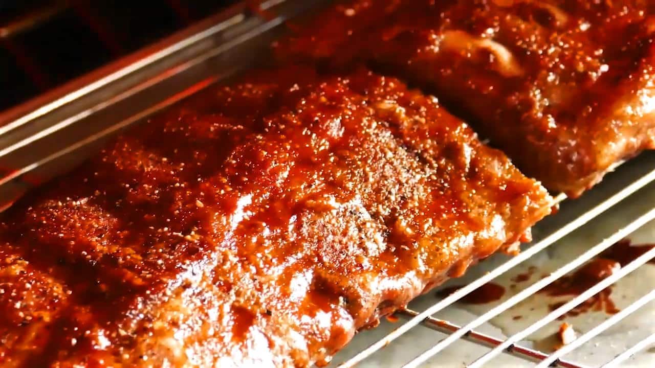 Ribs in oven on wire rack with BBQ sauce going under the broiler.