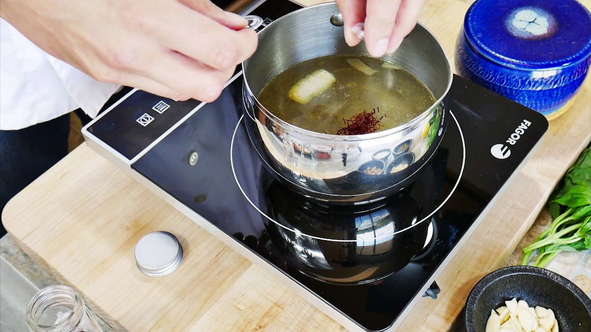 Prepare the Crab Stock. Action in image is adding saffron to the liquid.