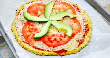 Cauliflower pizza with toppings of tomato sauce cheese fresh tomato and avocado.