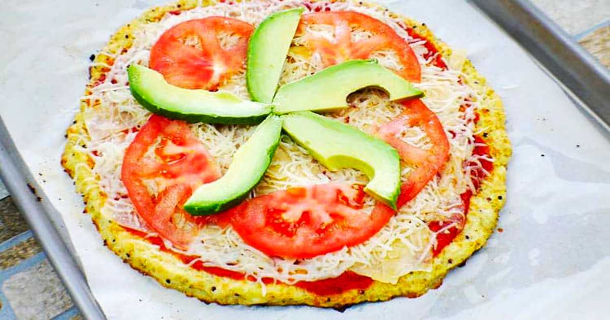 Cauliflower pizza with toppings of tomato sauce cheese fresh tomato and avocado.