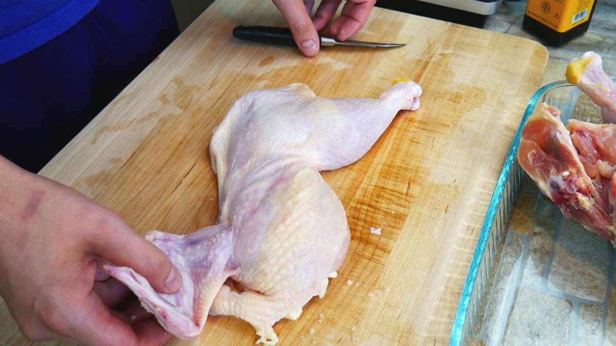 Half chicken, the thigh, leg and breast with skin on displayed on cutting board.