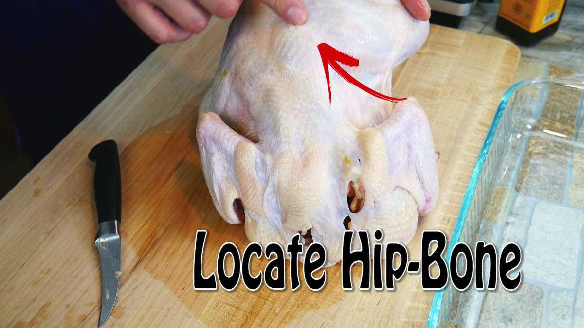 Chicken turned over with chef pointing at the location between the thighs and legs at the hip joint.