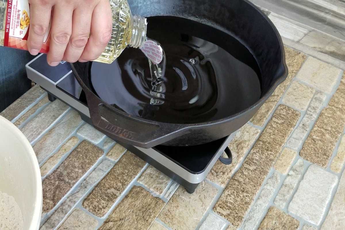 Peanut oil being poured into cast iron skillet.