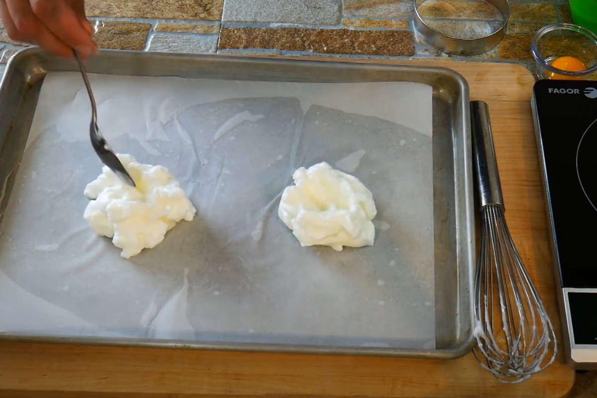 Shaping the whipped egg white on parchment paper molded into cloud shapes.