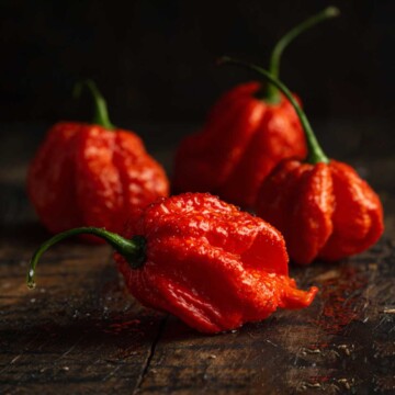 Red super hot chili peppers on dark wood surface showing wrinkled skin and stems.