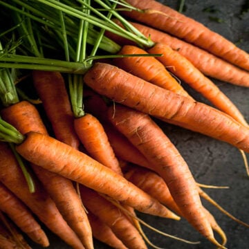 Orange carrots with green tops on a dark surface