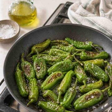 Fresh and blistered Padrón peppers in a skillet with flaky sea salt.
