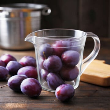 Plums in measuring cup on wooden table.