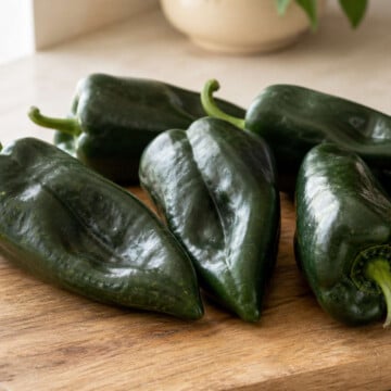 Fresh green poblano peppers on a wooden cutting board in morning window light.