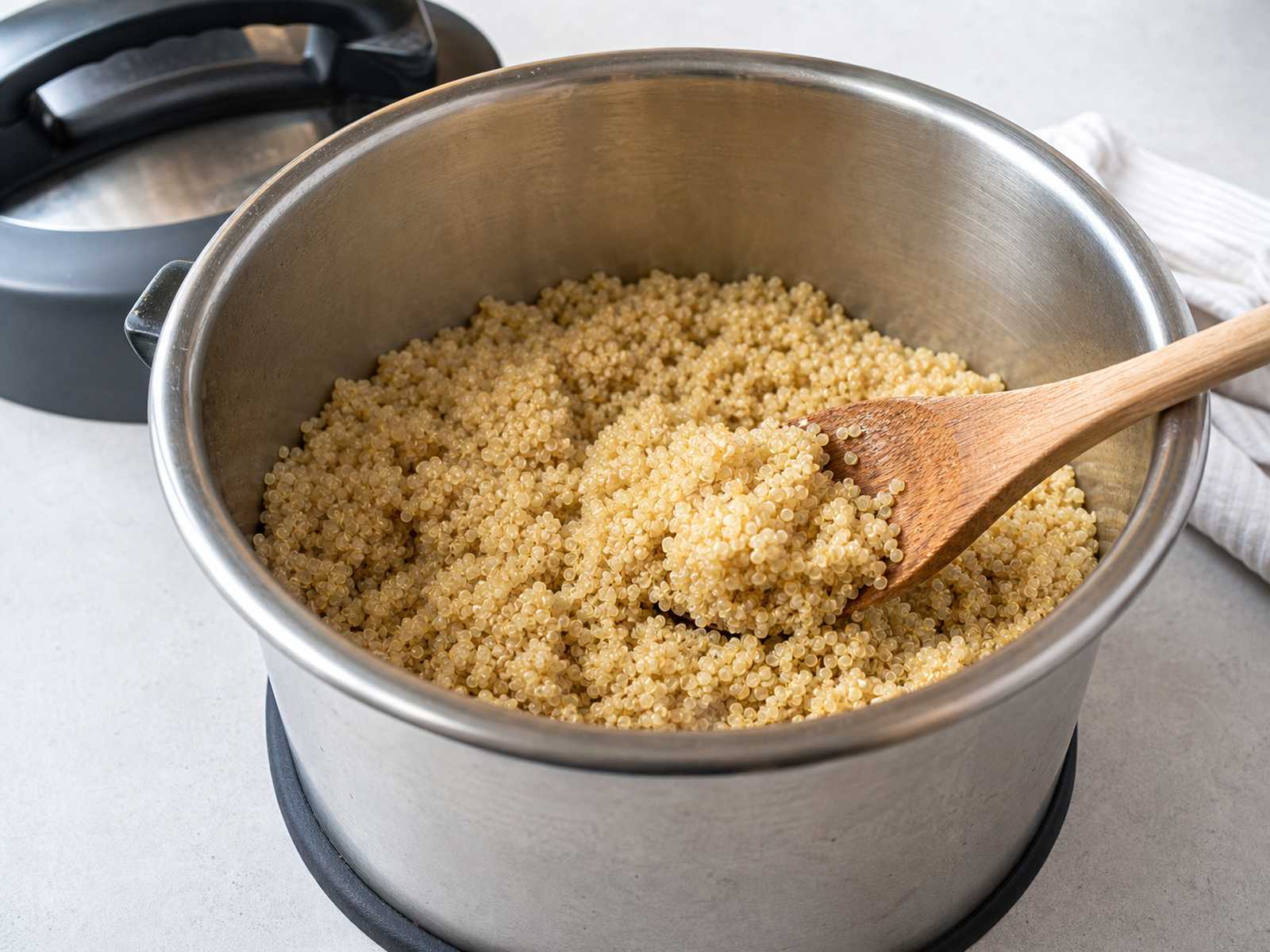 Fluffy cooked quinoa in a pressure cooker insert with a wooden spoon.