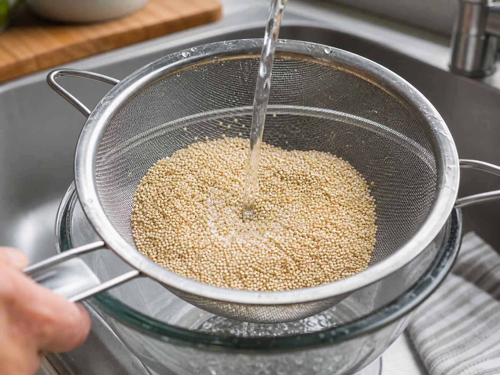 Uncooked quinoa being rinsed in a fine mesh strainer before cooking.