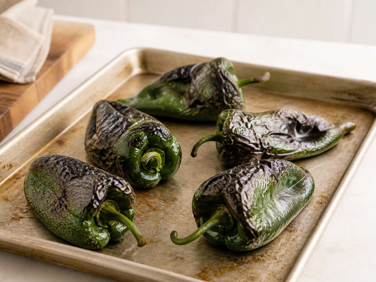 Roasted poblano peppers with blistered skin on a sheet pan